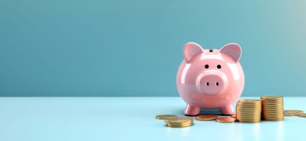 Pink pig piggy bank next to a stack of gold coins, isolated on blue background. Investment success,